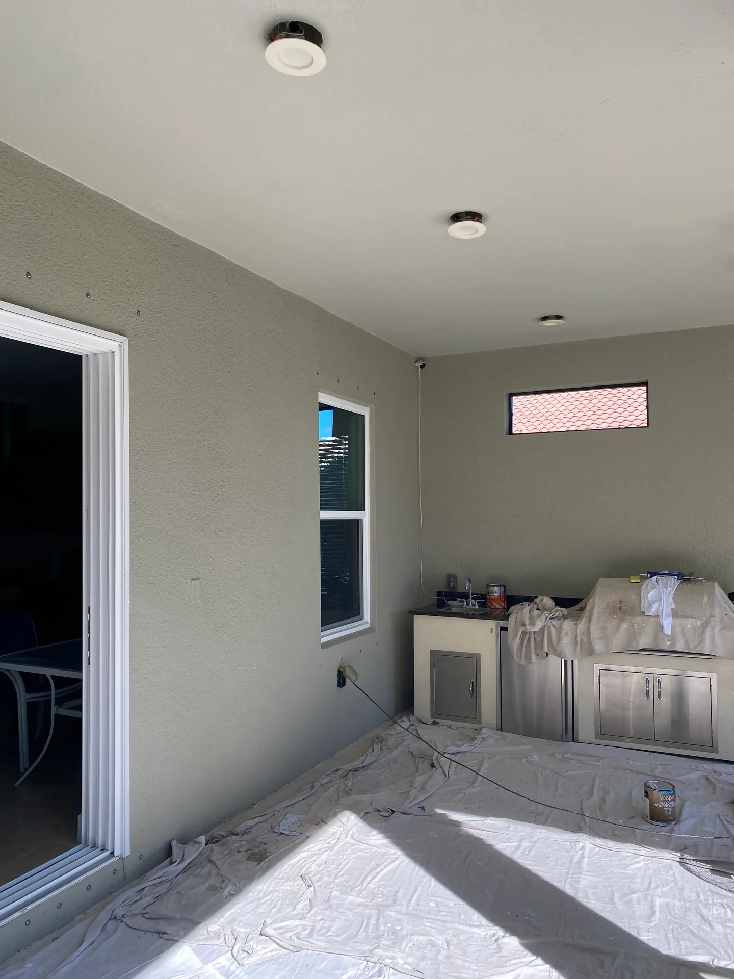 Interior room with sage green walls being repainted, stainless appliances and cabinets masked with plastic sheeting