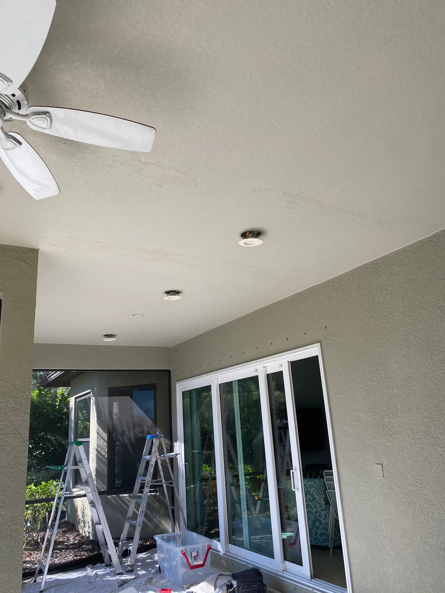 Interior room mid-painting with freshly coated greige walls and ceiling, a ladder, and drop cloths protecting the floor